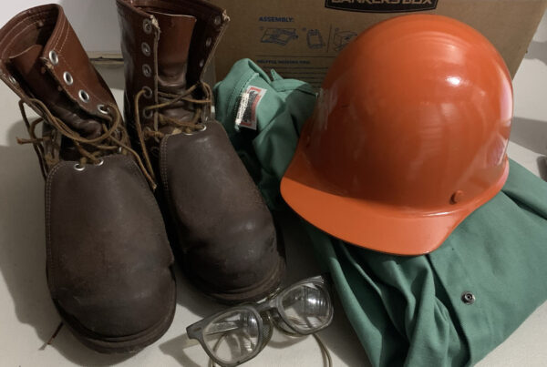brown, steel toed boots, a orange hard hat, greens protective wear, and safety glasses.