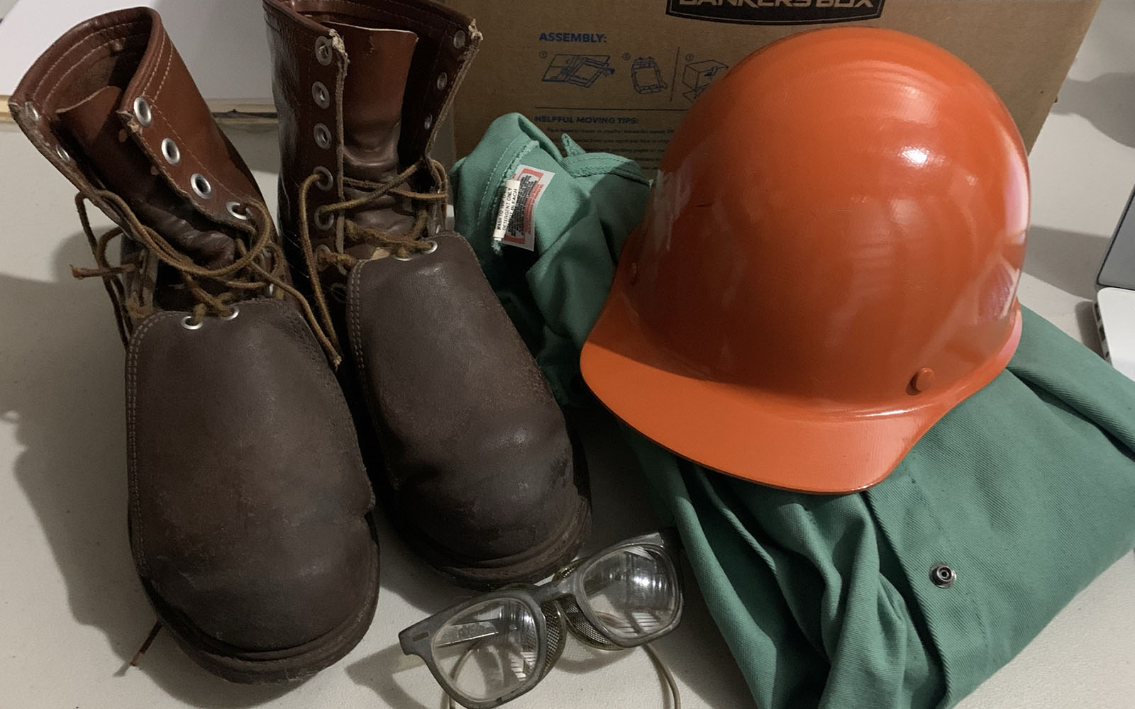 brown, steel toed boots, a orange hard hat, greens protective wear, and safety glasses.