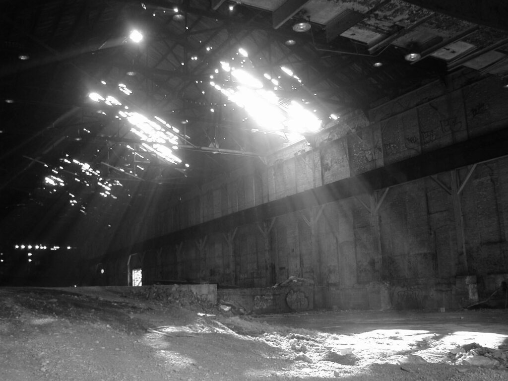 A black and white image of sun coming through holes in the roof of the Power House.