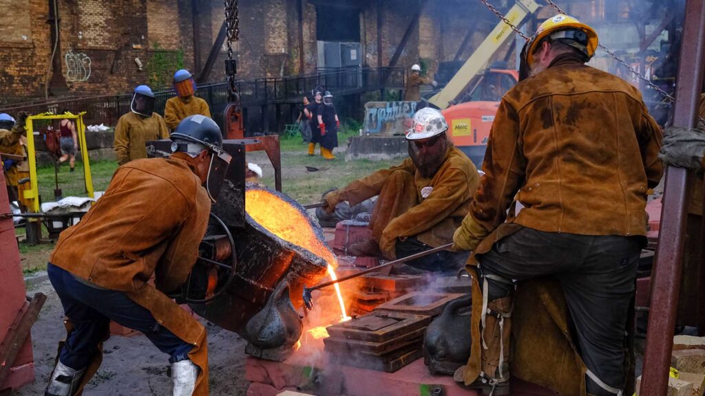 Three iron workers pour hot metal into molds.
