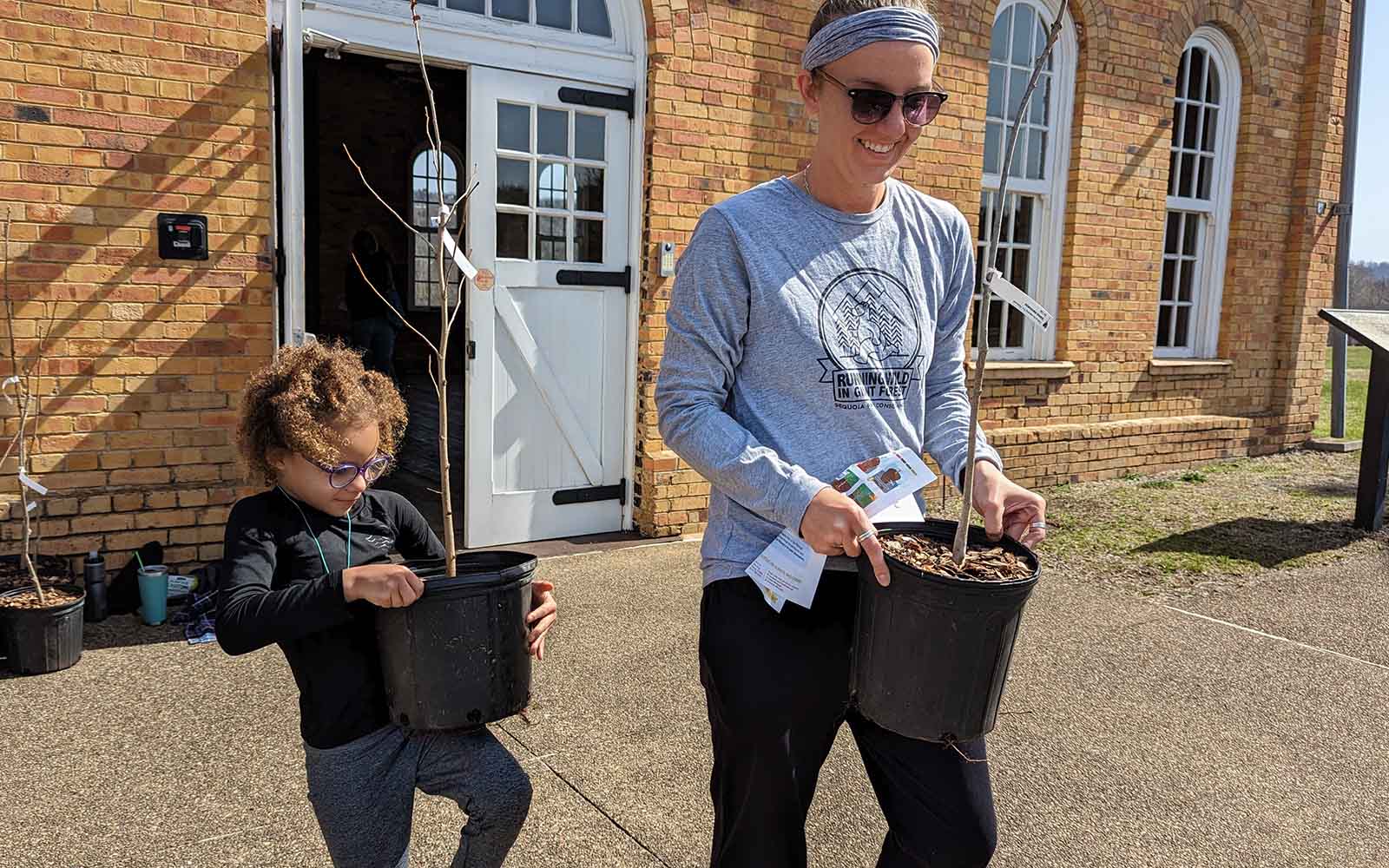 A white mom and her biracial daughter carry trees.