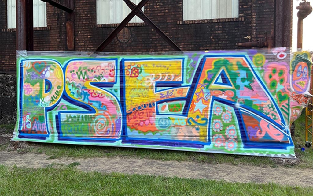 A temporary spray-painted mural colorfully reads P S E A.