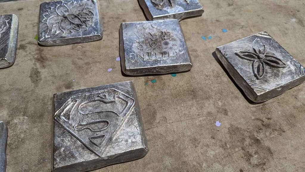 Six aluminum tiles sit on a table. One displays the Superman symbol.