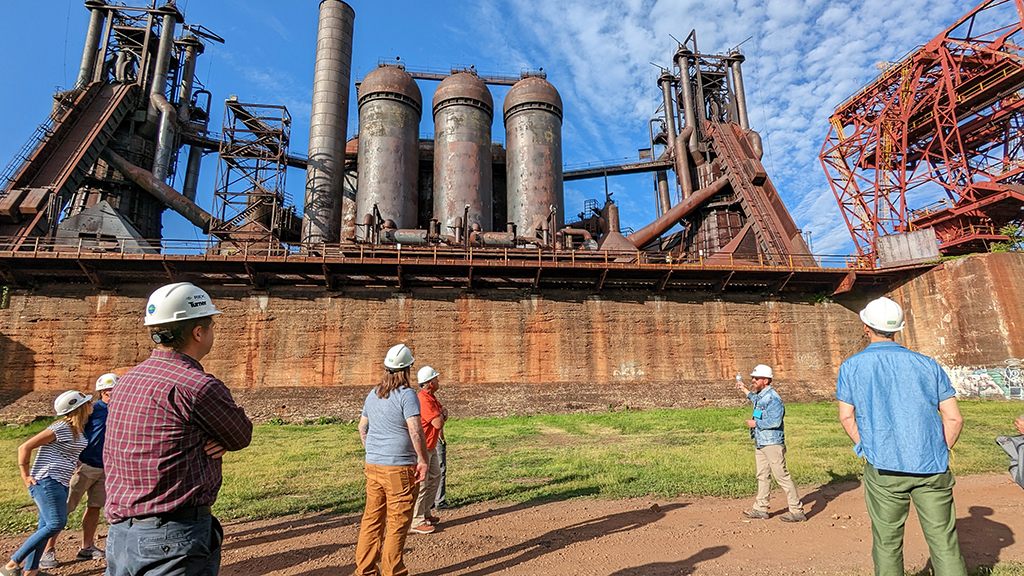 The tour passes through the Ore Yard and guests look up at the stoves, stack, and furnaces. 