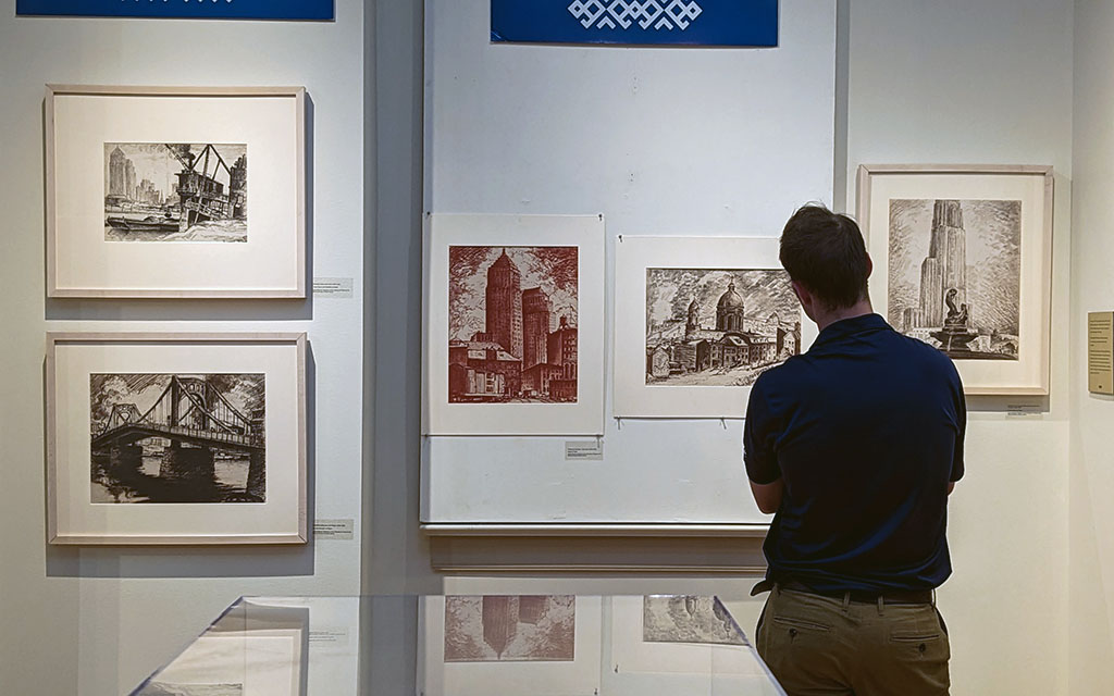 A man looks at a wall of sketches of Pittsburgh, including bridges and the Cathedral of Learning.
