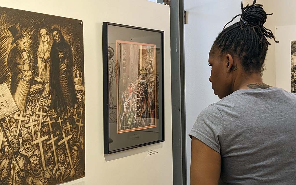 A black woman with braids in a gray t-shirt looks a provocative religious artworks.