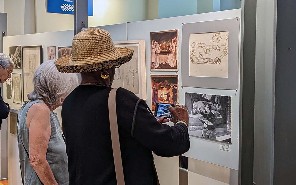 A black woman in a hat takes a photo of a photograph of Maxo Vanka.