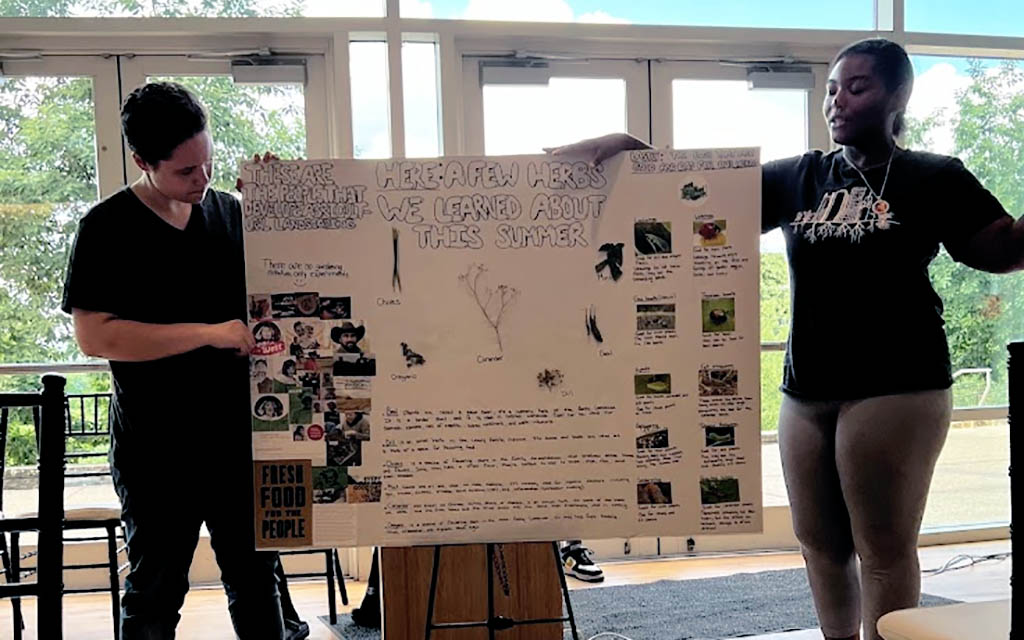 Two teens display a presentation board with information about herbs.