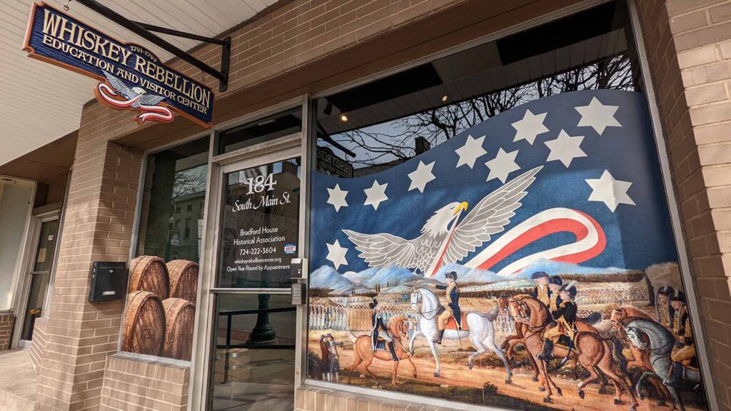 The façade of the Whiskey Rebellion Visitors Center, a storefront with 17th century stars, stripes, and eagle style art in the window.