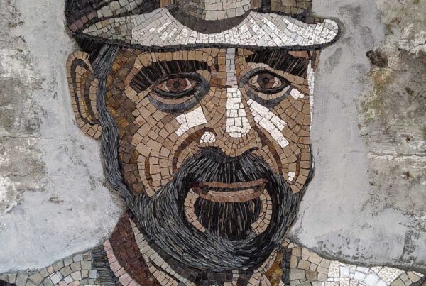 Detail of A mosaic image of a miner with a light on his forehead wearing a jacket with lapels. The lines of the image contour the shape of this face, goatee, and curvature of his chest.