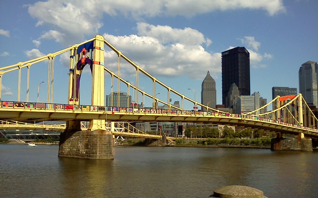 One of Pittsburgh's iconic yellow bridges is shown lined with knitted work created by volunteers.