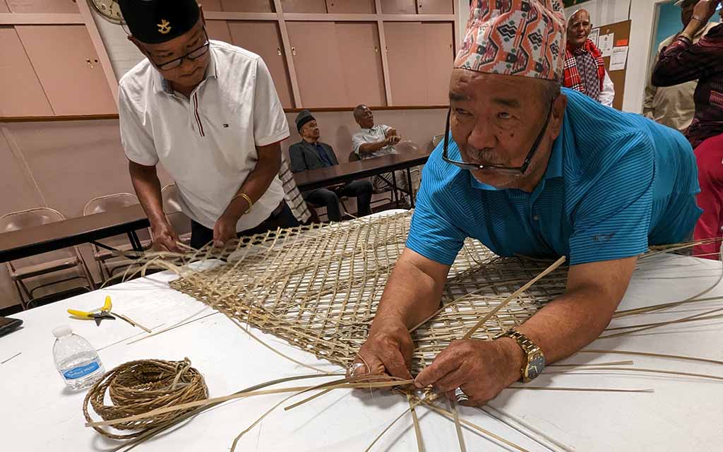 Two men in hats work at weaving reeds.