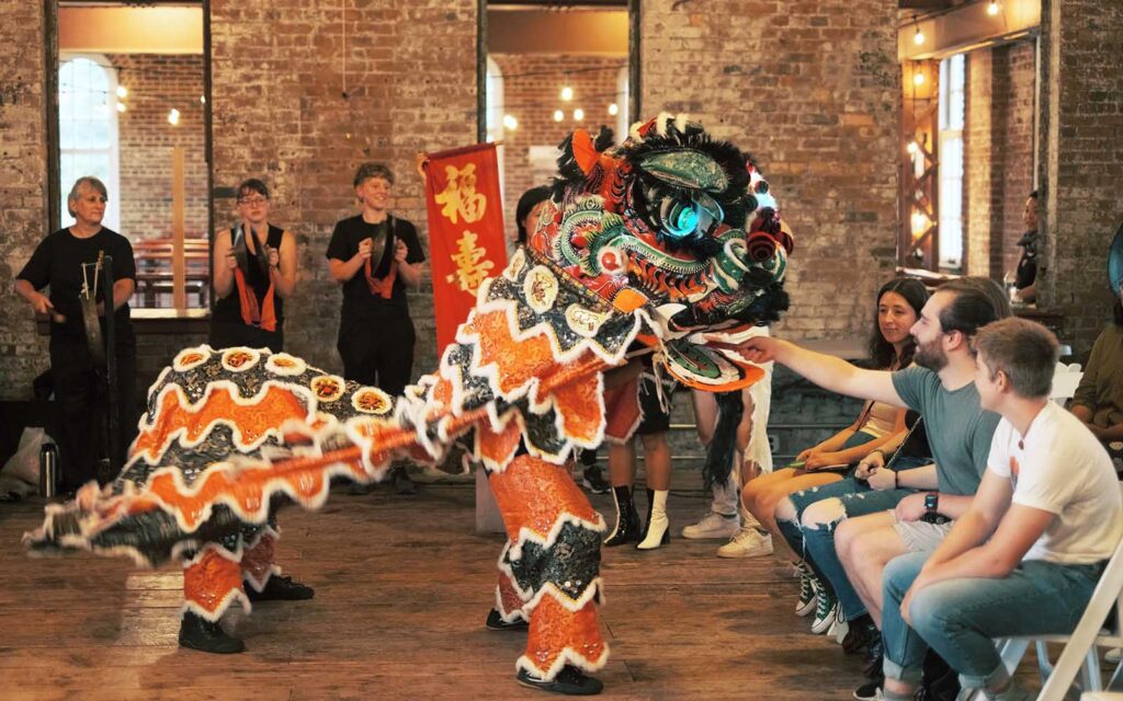 A Chinese dragon dance is performed in the brick-walled Pump House for a crowd seated in folding chairs.