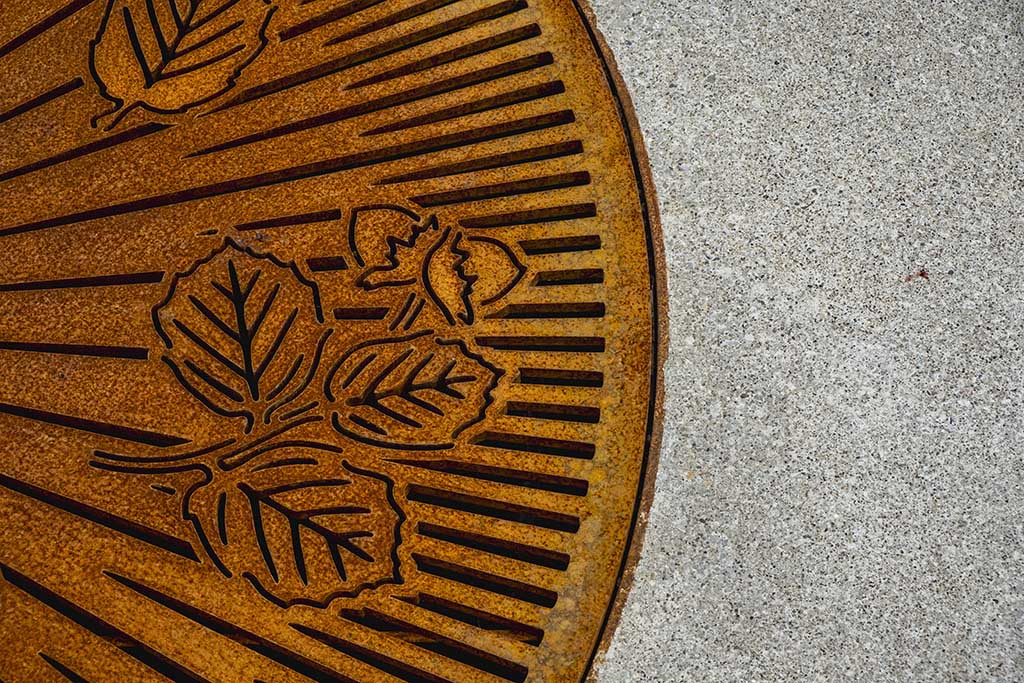 An intentionally rusted tree grate has radiant lines and hazelnut leaves in the negative space for water to flow. 