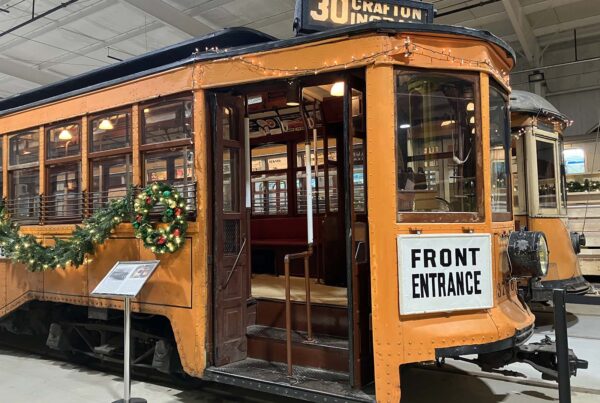 An orange trolley with an open door is decorated for the holidays with lit garlands.