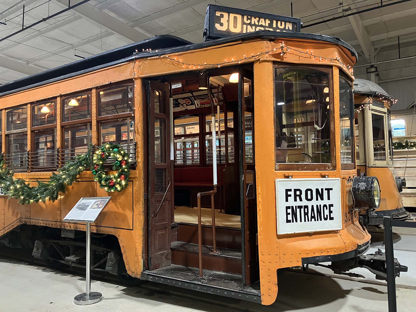 An orange trolley with an open door is decorated for the holidays with lit garlands.