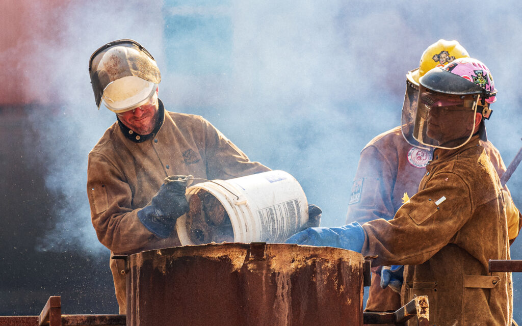 Artists pour coke and limestone into the top of the iron furnace during an iron casting workshop