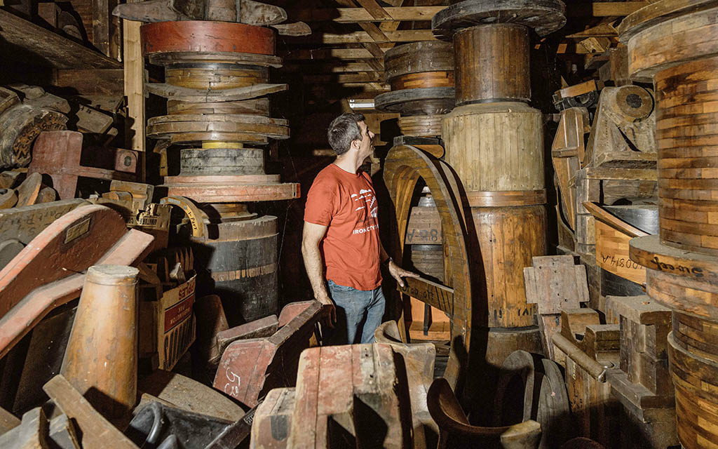 Foundry patterns are stacked floor to ceiling in a barn. A man looks around in the middle of the image.