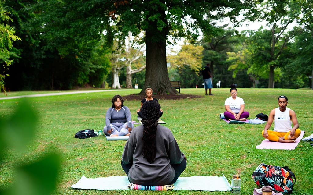 Five black people practice yoga in a park