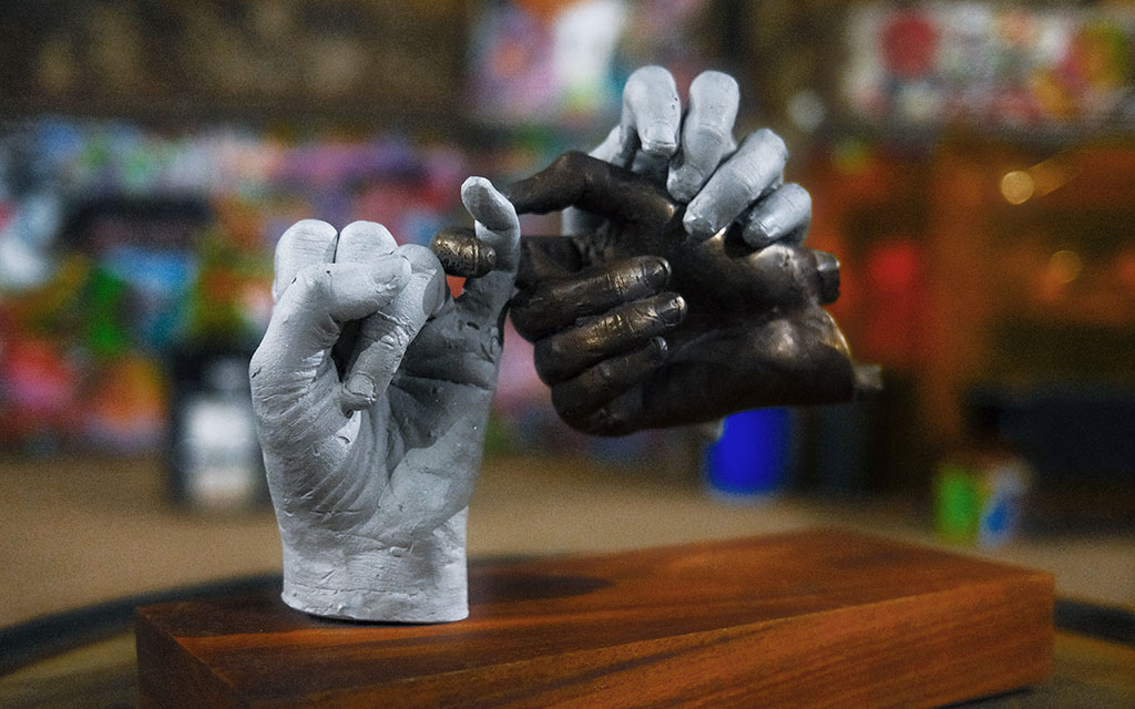 A sculpture of three hands, two are silver and one is dark.