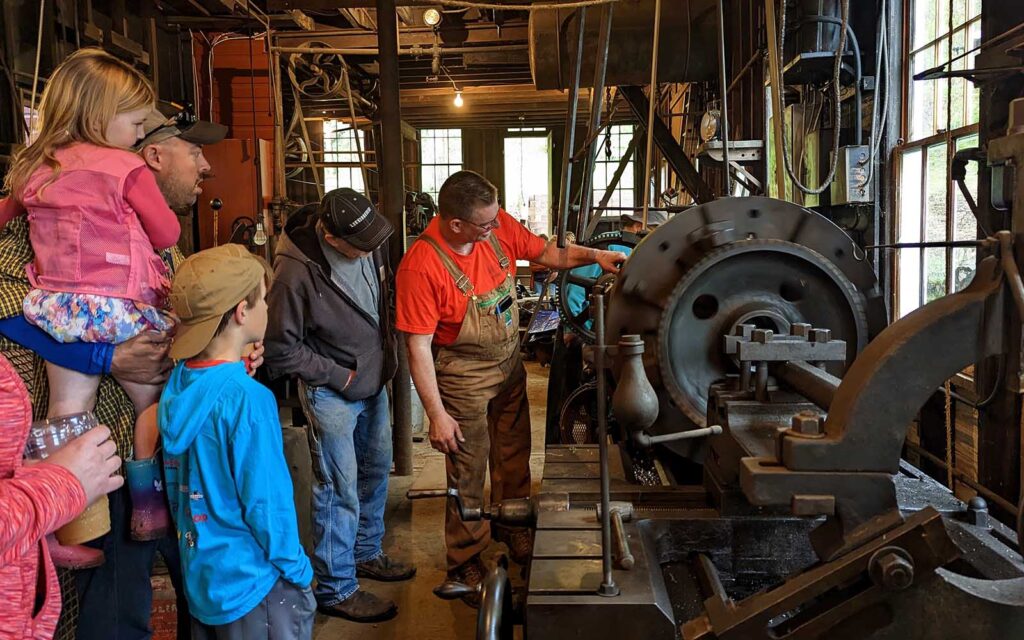 A multigeneration family tours the machine shop as a guide demonstrates how a machine works.