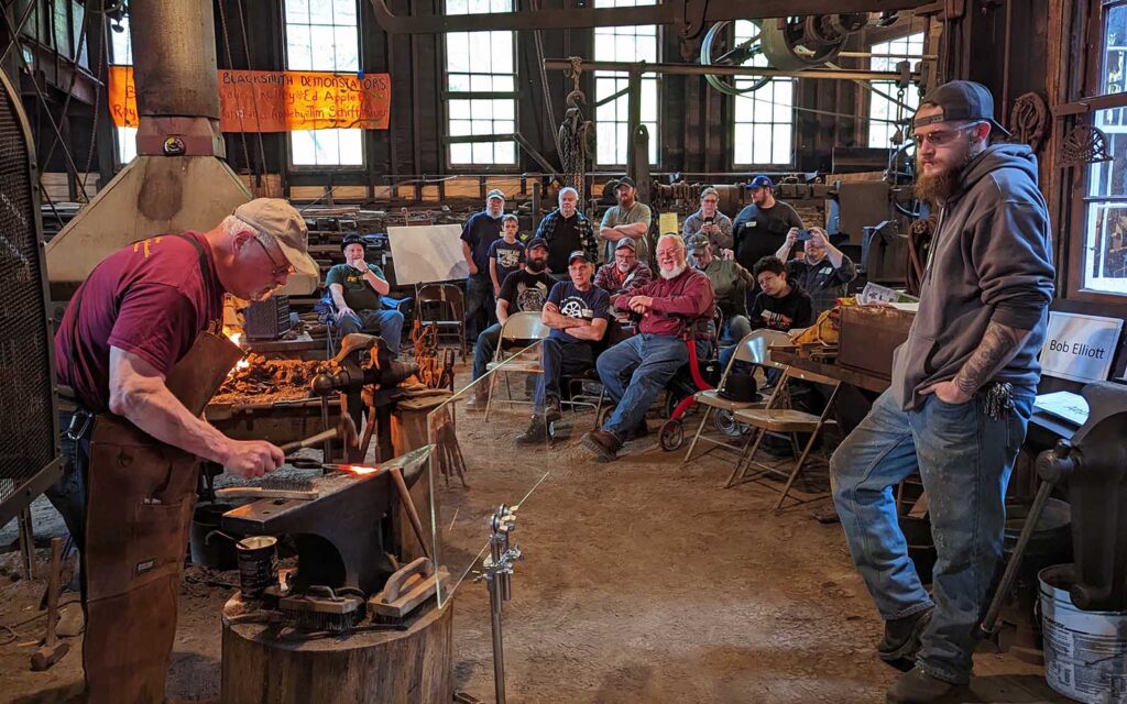 A blacksmith works in front of a crowd.