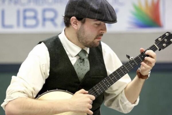 A banjo player wearing a vest and cap.