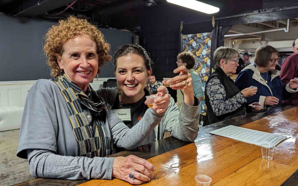 Two tour guide raise their drinks for a toast and smile at the camera.