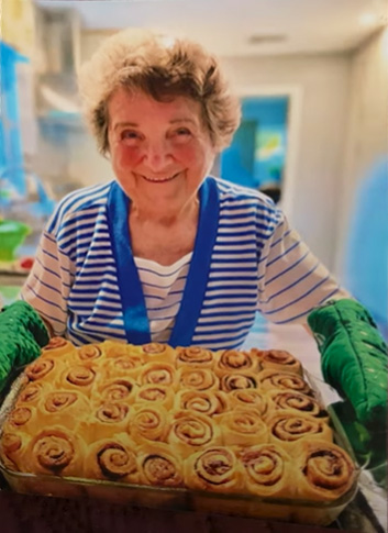 A graying woman wearing oven mitts hold out a tray of food.