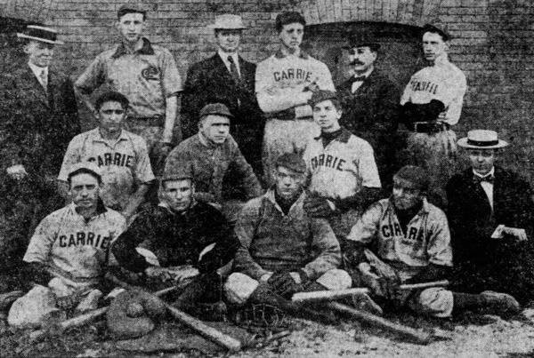 A black and white team photo of a baseball club wearing jerseys that say Carrie with men in suits and flat brim hats standing with the players.