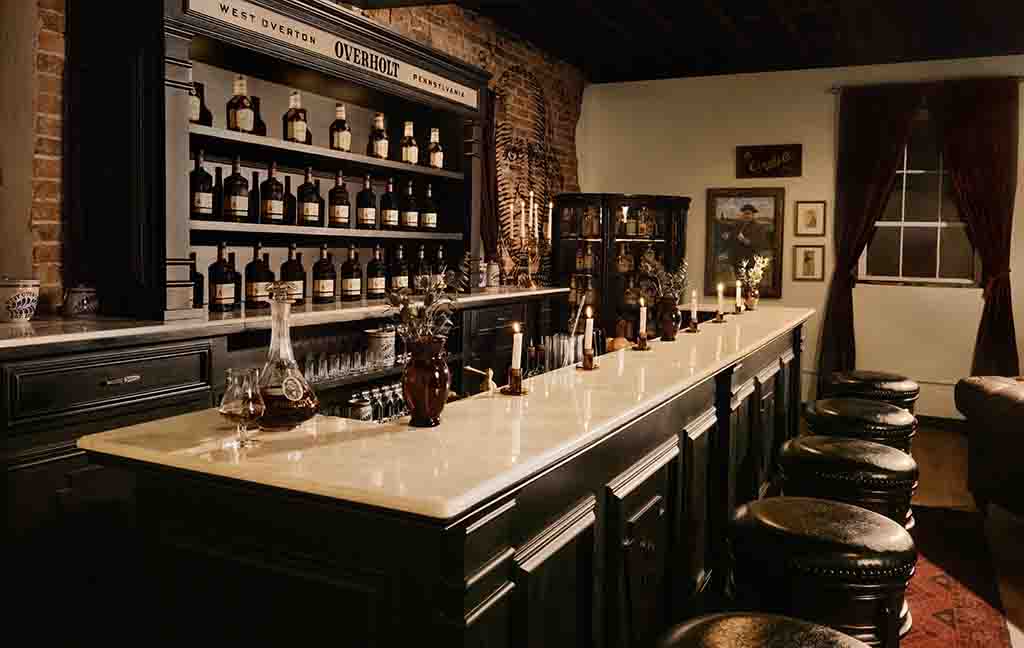A black wooden bar with a black, bottle lined shelves is contrasted by a marble bartop.