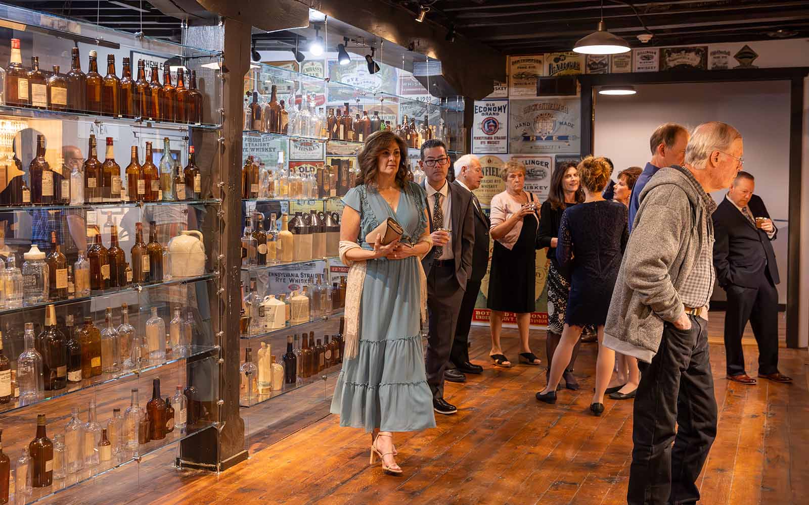 Guests mill around in a gallery with a wall of booze bottles in dressy clothes.