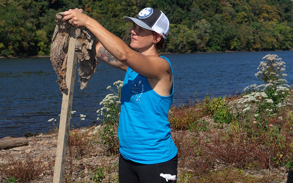 A woman in a tank shirt and trucker hat arranges something on a post.