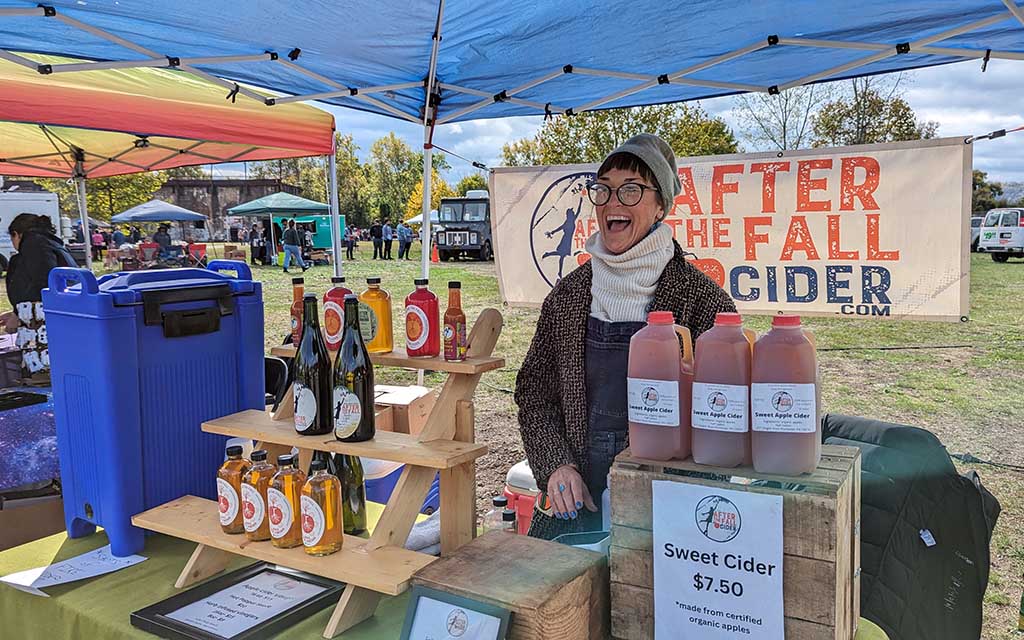 A woman sells cider under a tent.