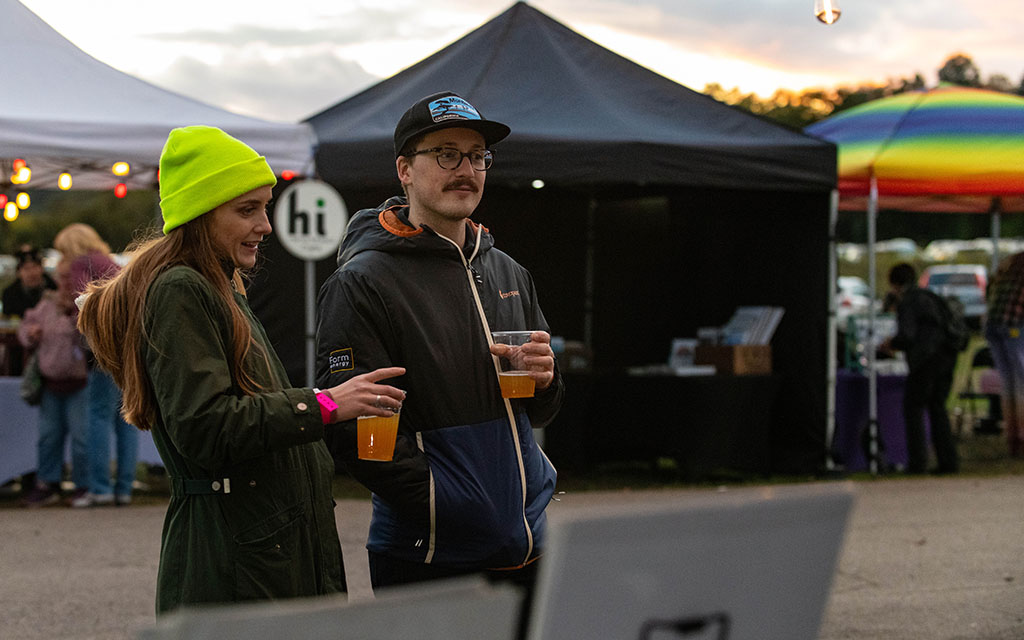 A couple, each holding a beer, looks at vendor merch.