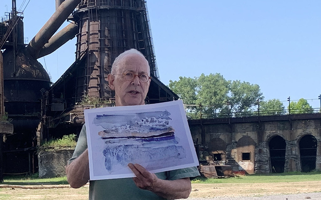 a man holds up a sketch with the furnace behind him