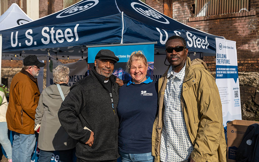 Two black men and a white woman post for the camera in front of the U.S. Steel tent.