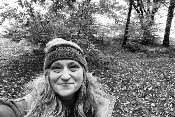 a black and white selfie of a woman with a knit cap on in the woods.