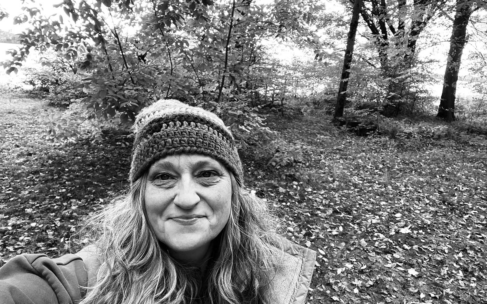 a black and white selfie of a woman with a knit cap on in the woods.