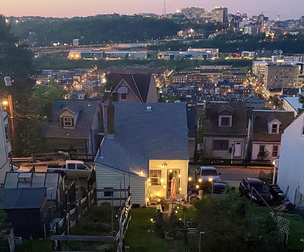 A twilight view of a house on a hill that overlooks other homes and the Oakland neighborhood of Pittsburgh from across the river.