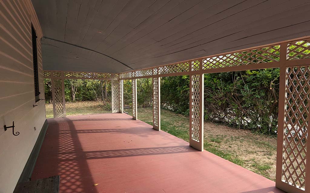 A red painted porch covered by a roof with the ceiling painted blue, and supported with lattice work uprights.