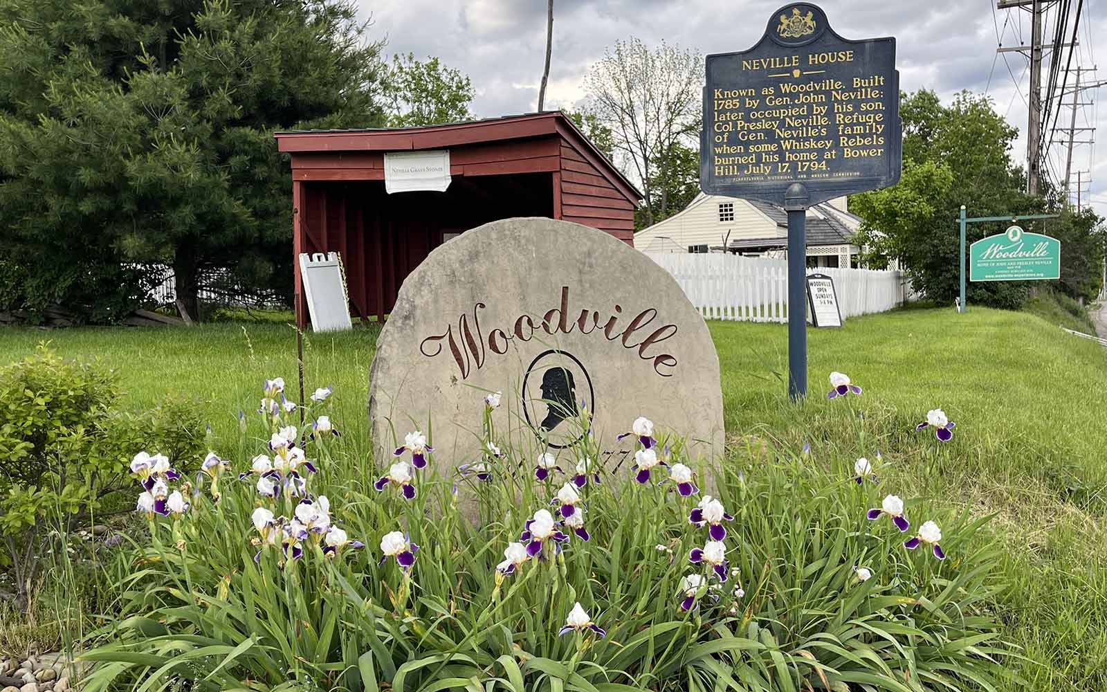 A stone sign situated in the grass with flowers around it reads Woodville.