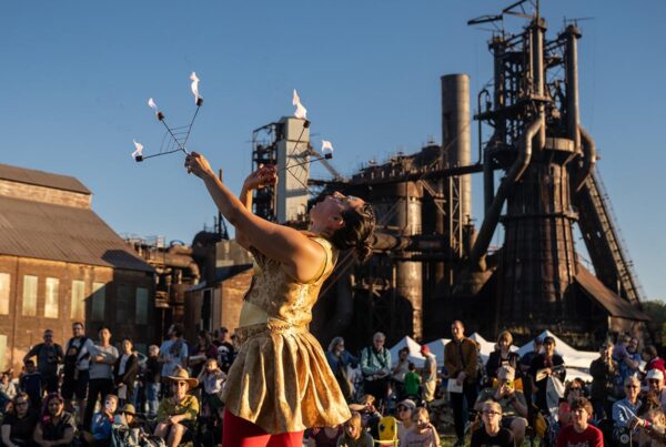 A flame performer in front of a crowd with Carrie in the background.