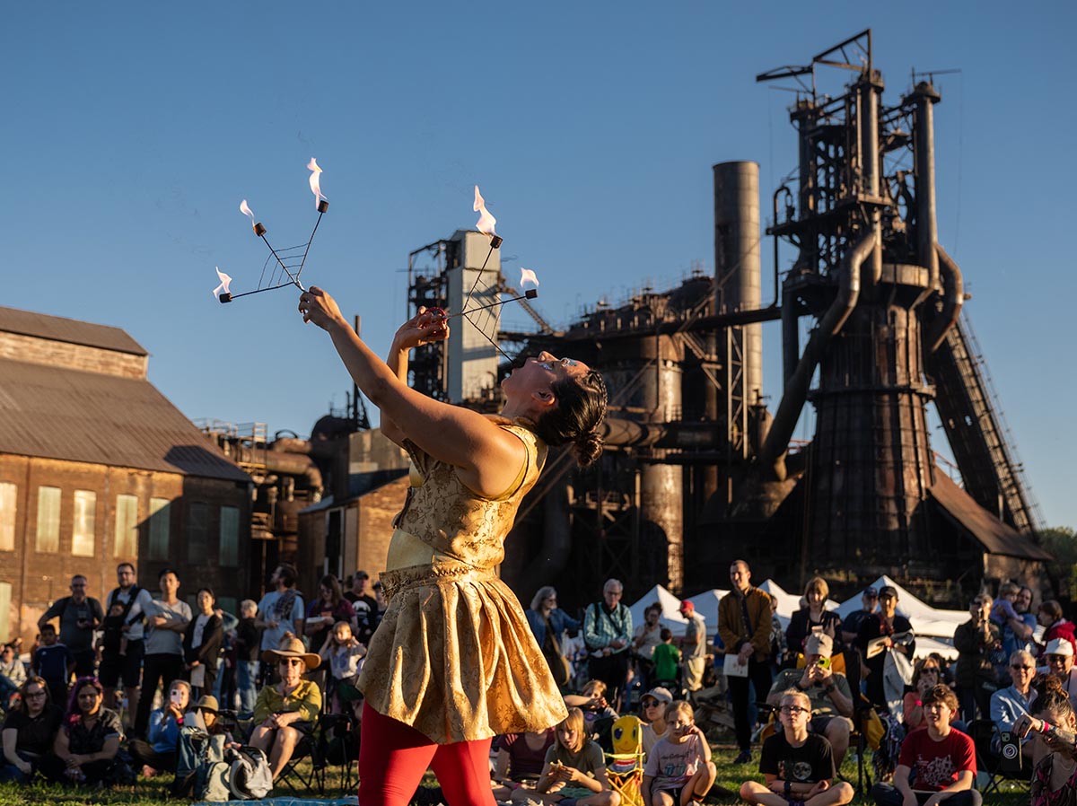A flame performer in front of a crowd with Carrie in the background.