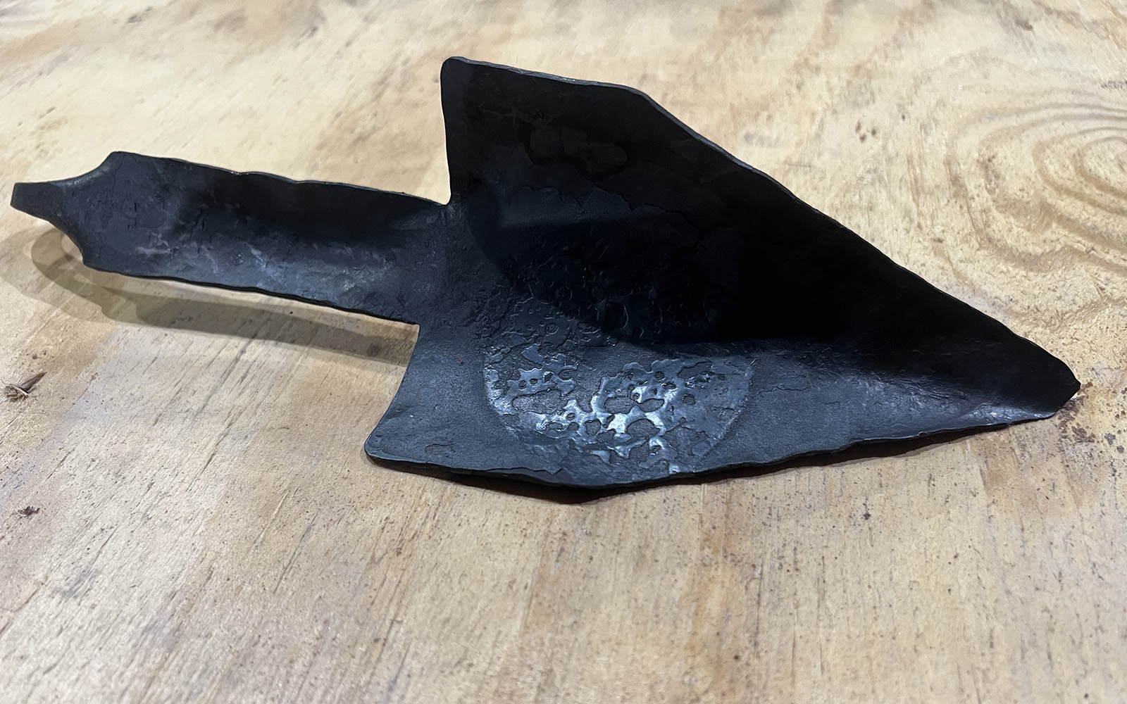 image shows a forged trowel sitting on wooden base.