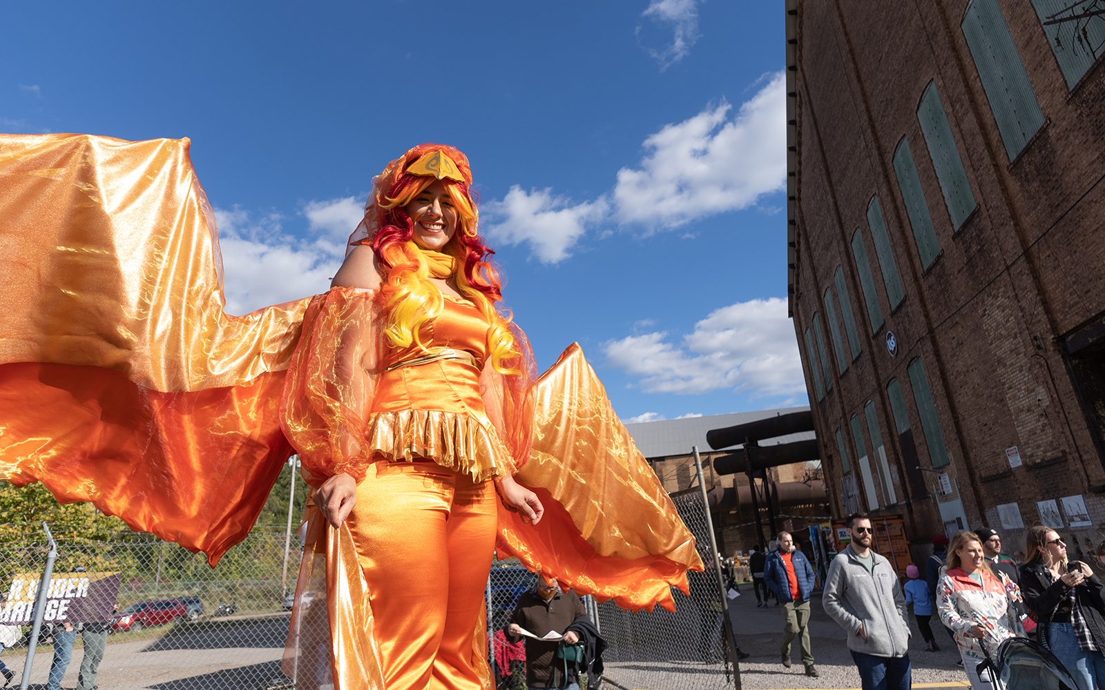 A woman dressed in an orange phoenix costume stands in the foreground of the Festival of Combustion at Carrie Furnaces.